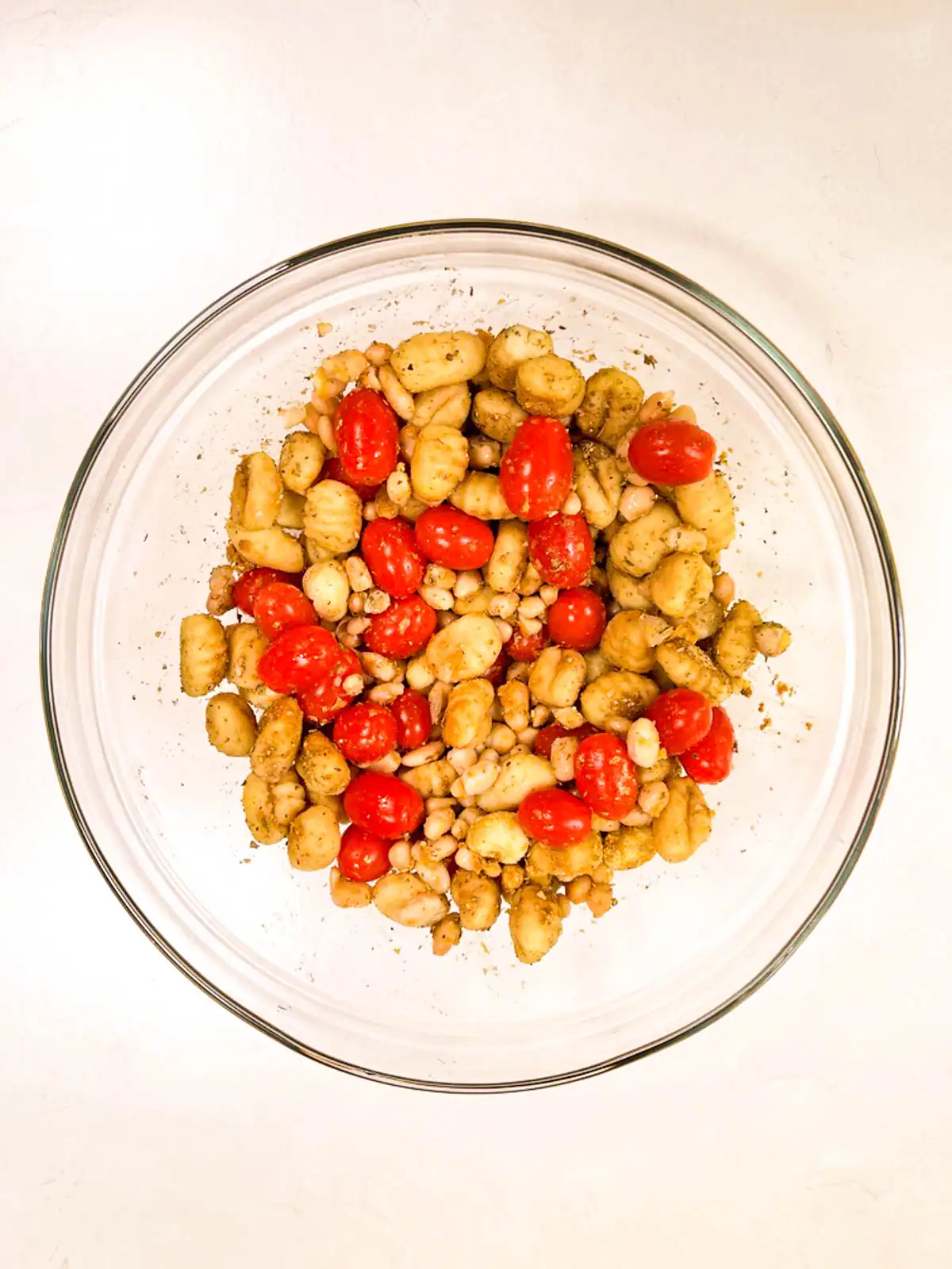 Gnocchi with tomatoes, white beans, and seasoning in a glass bowl.