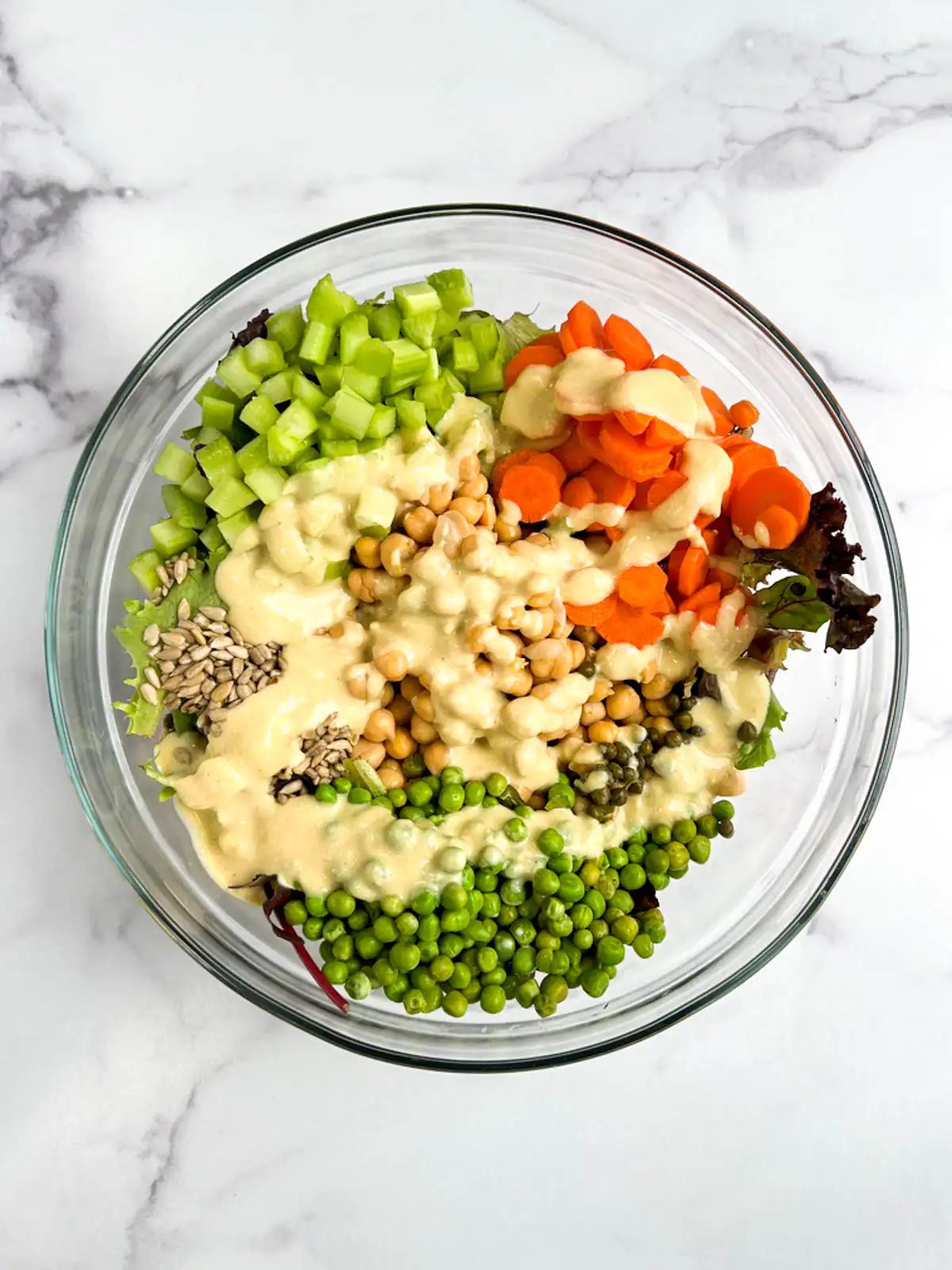 Chickpea veggie salad topped with vegan Caesar dressing in a glass bowl.
