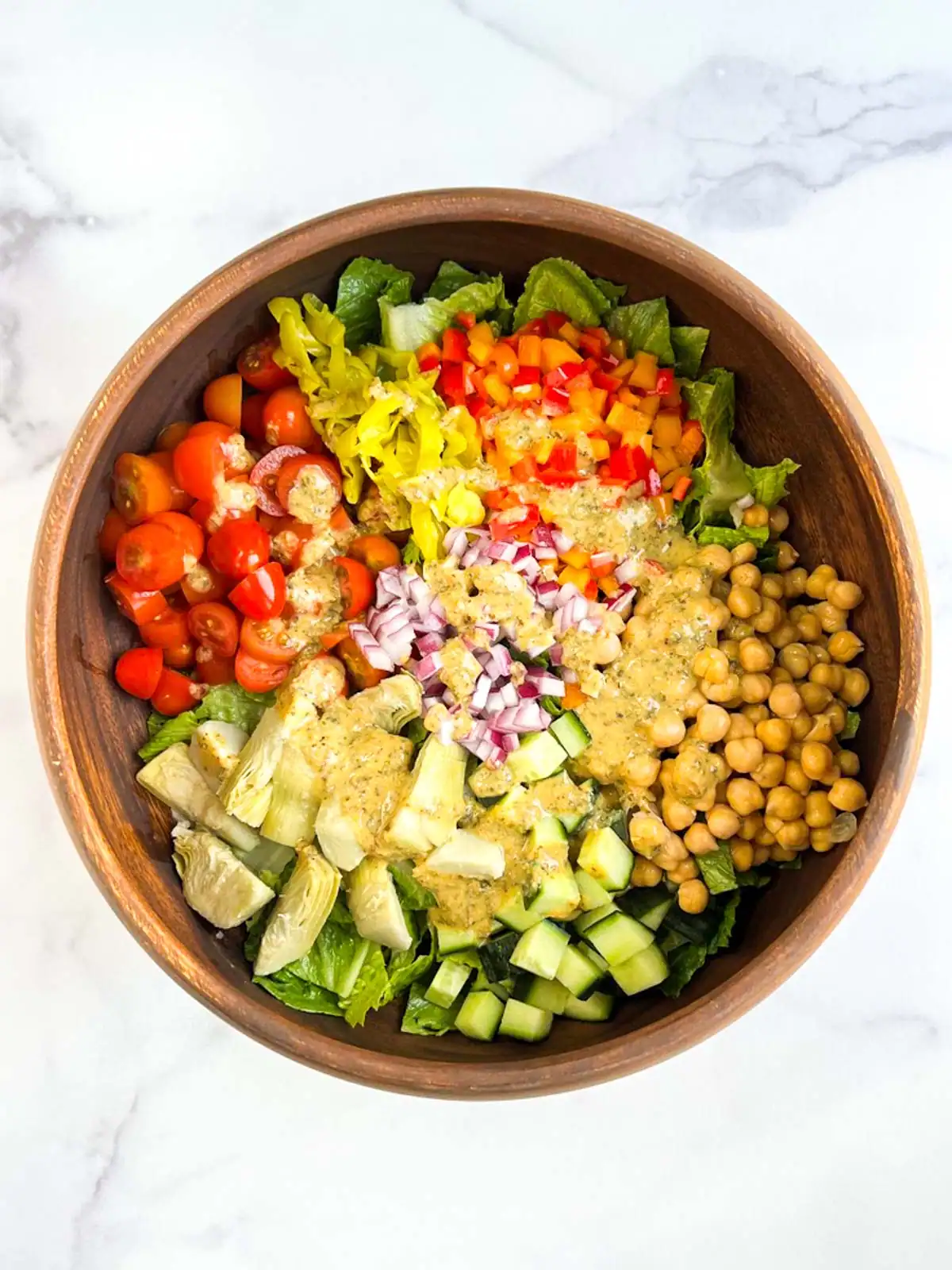 Ingredients for vegan Italian chopped salad topped with oil-free Italian dressing in a wooden bowl.