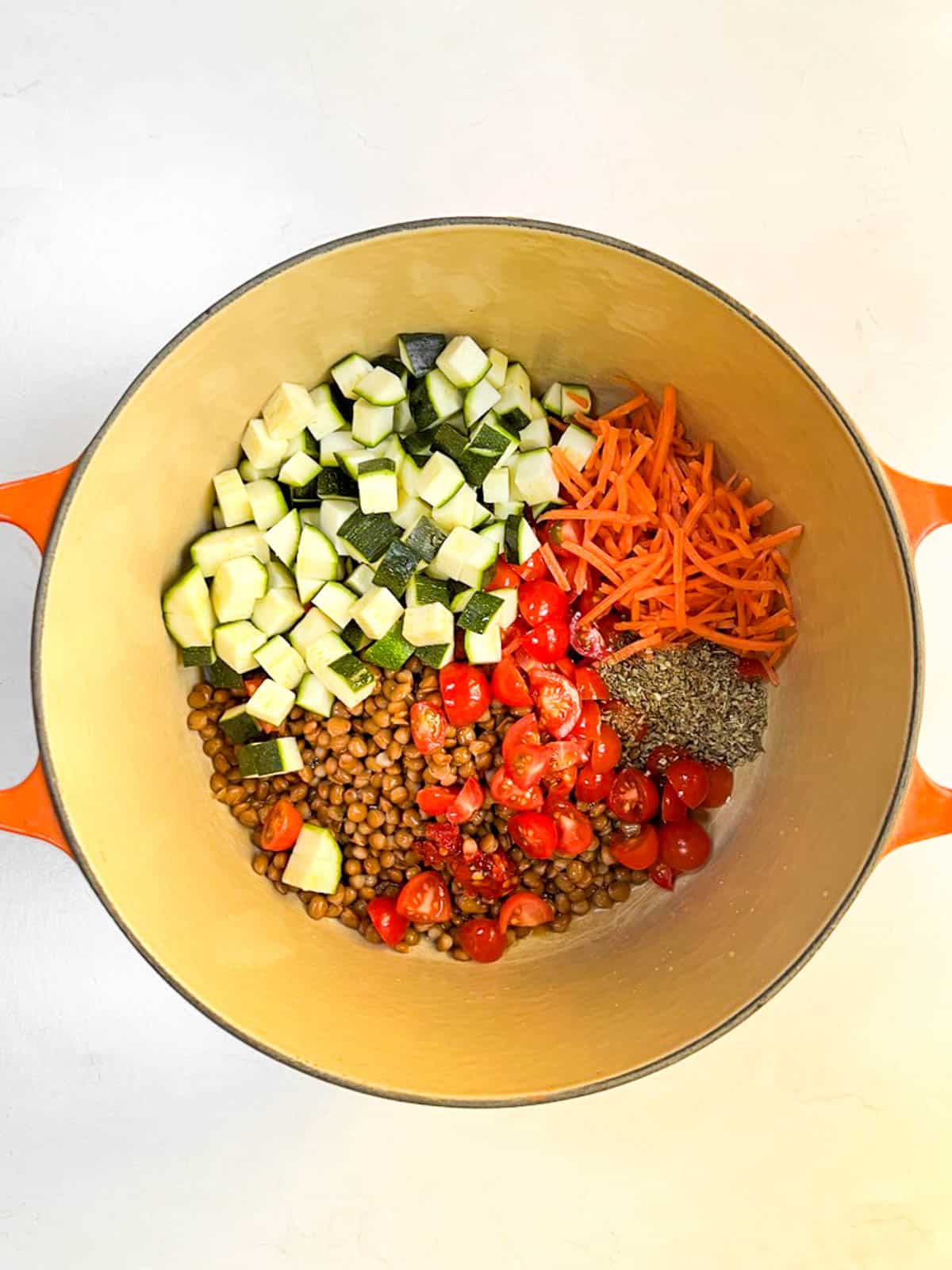Uncooked vegetables, lentils, and seasoning in a pot.