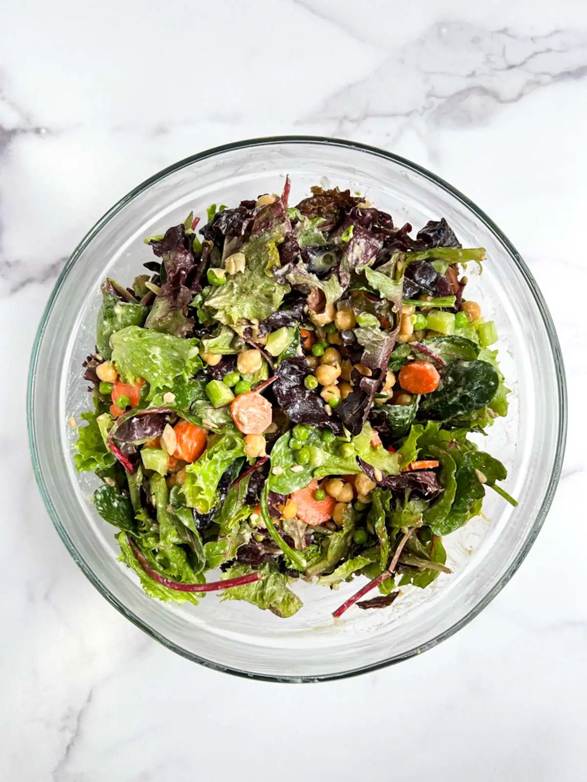 Chickpea veggie salad tossed with vegan Caesar dressing in a glass bowl.