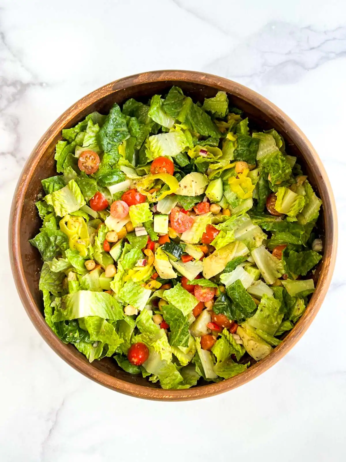 Oil-free vegan Italian chopped salad in a wooden bowl on a marble surface.