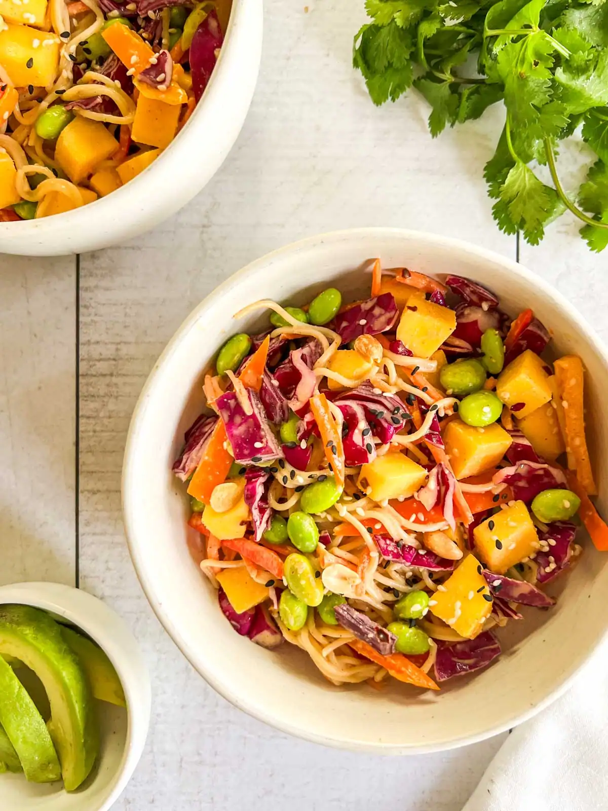 Mango peanut noodle salad in a bowl with fresh cilantro and avocado.