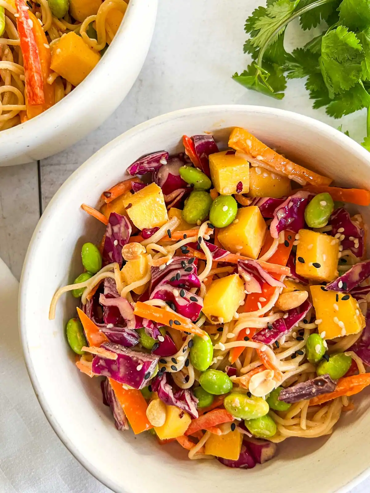 Mango peanut noodle salad in a white bowl with fresh cilantro.