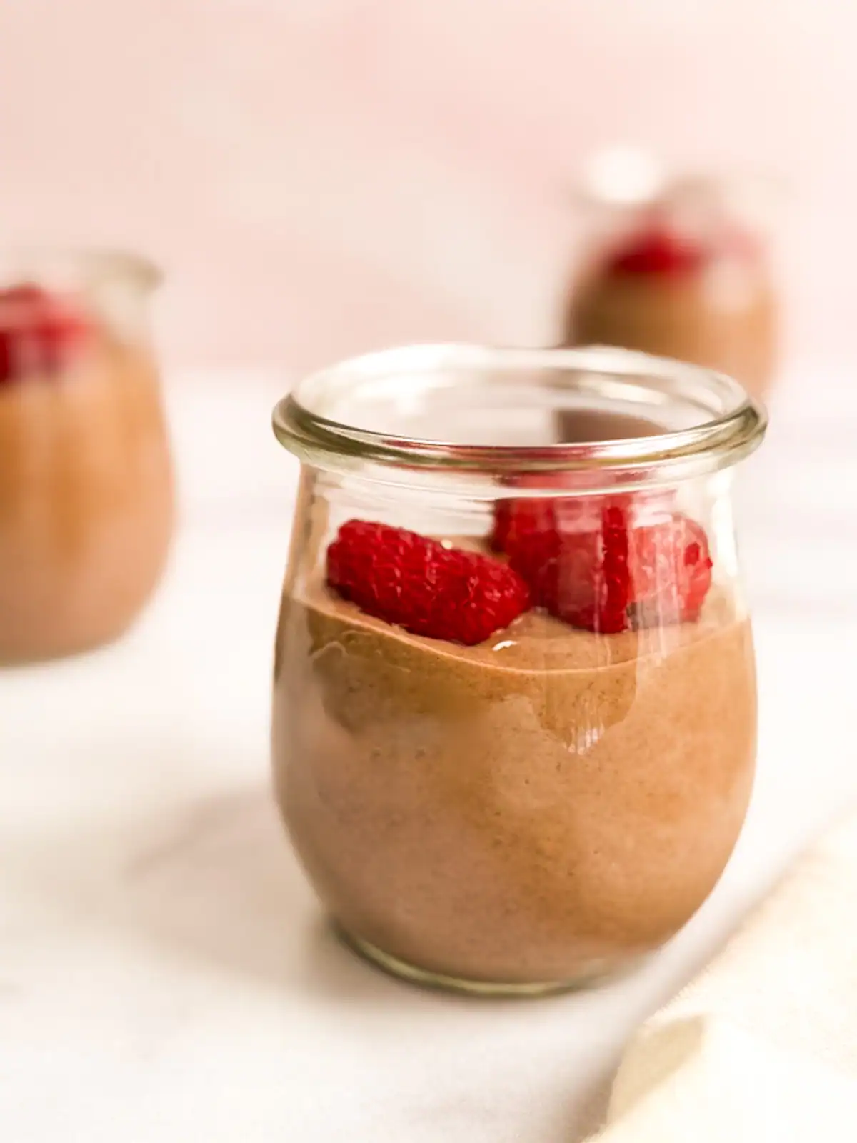 Vegan chocolate mousse topped with raspberries in small glass jars.