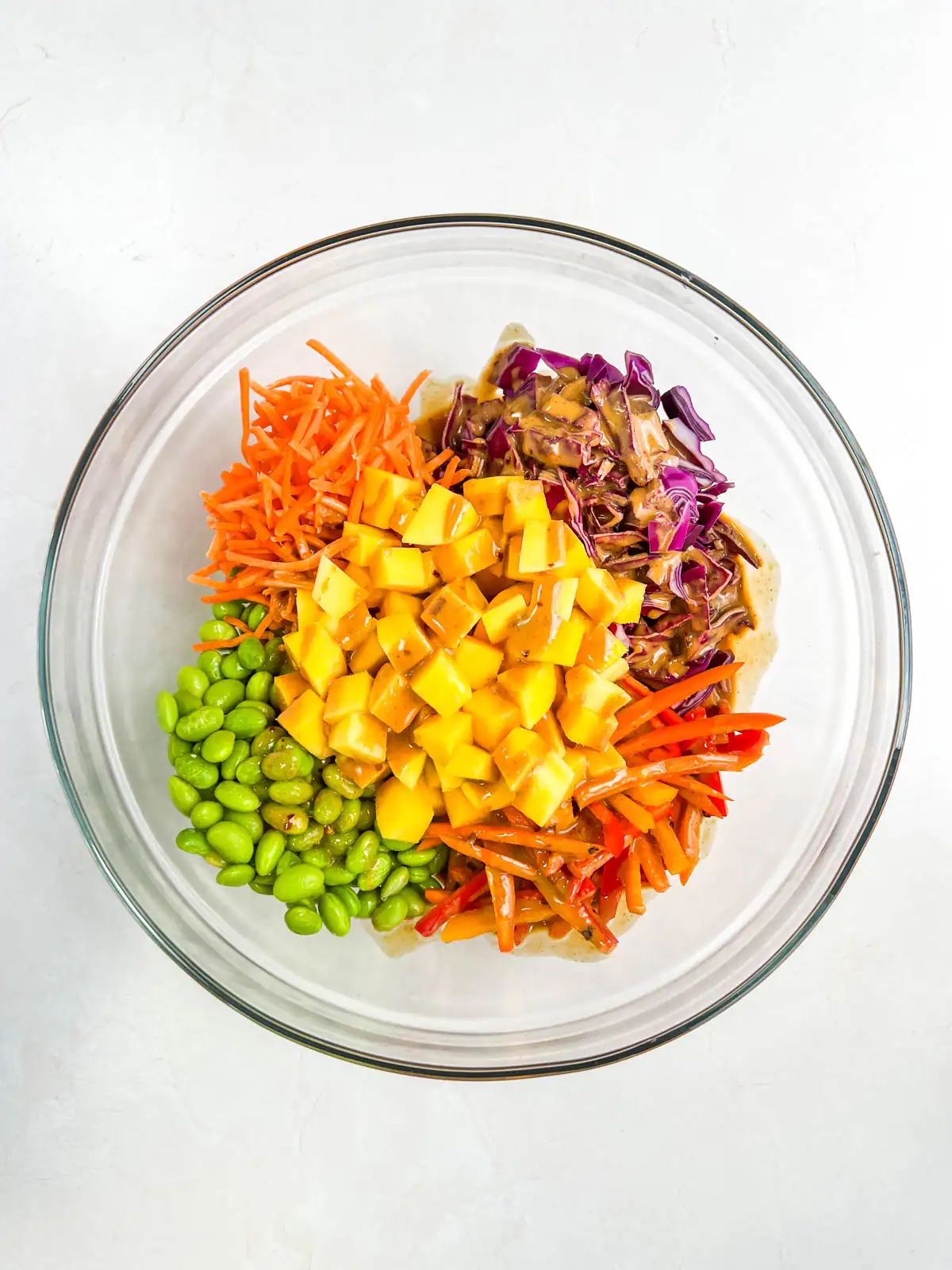 Ingredients for mango peanut noodle salad topped with peanut dressing in a glass bowl.