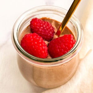 Vegan chocolate mousse topped with raspberries in a small glass jar.