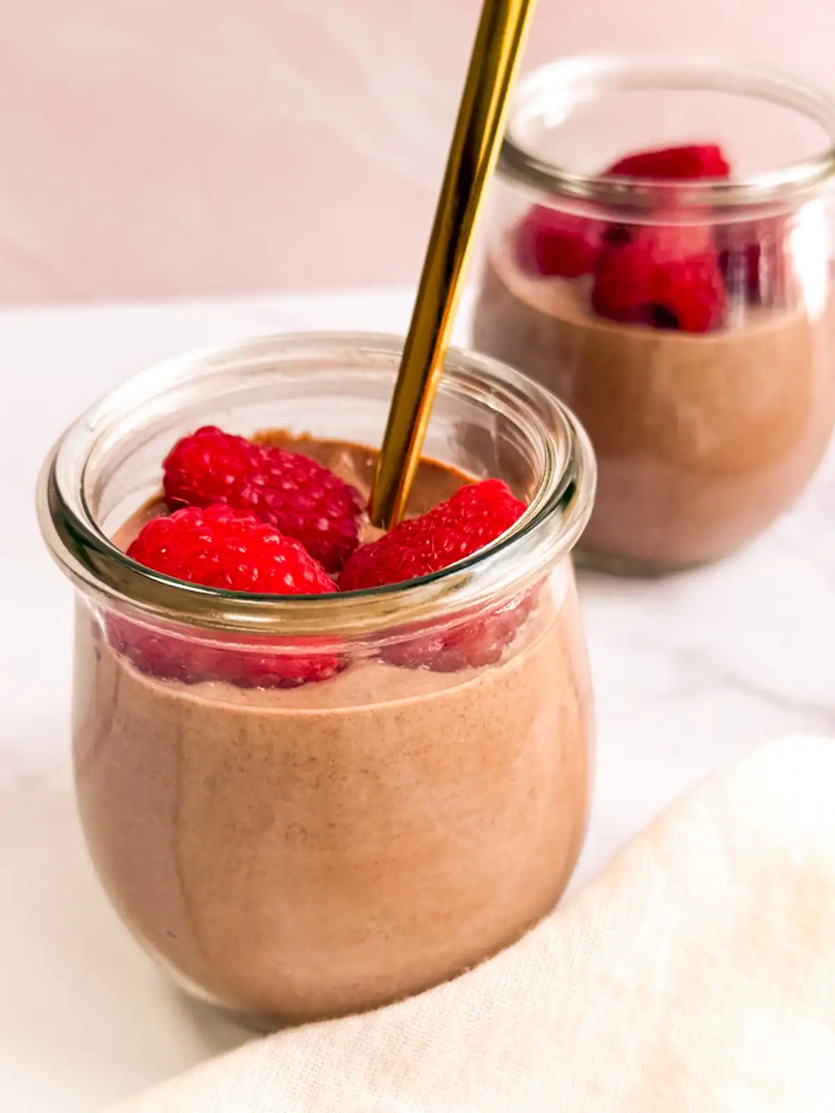 Vegan chocolate mousse topped with raspberries in small glass jars.