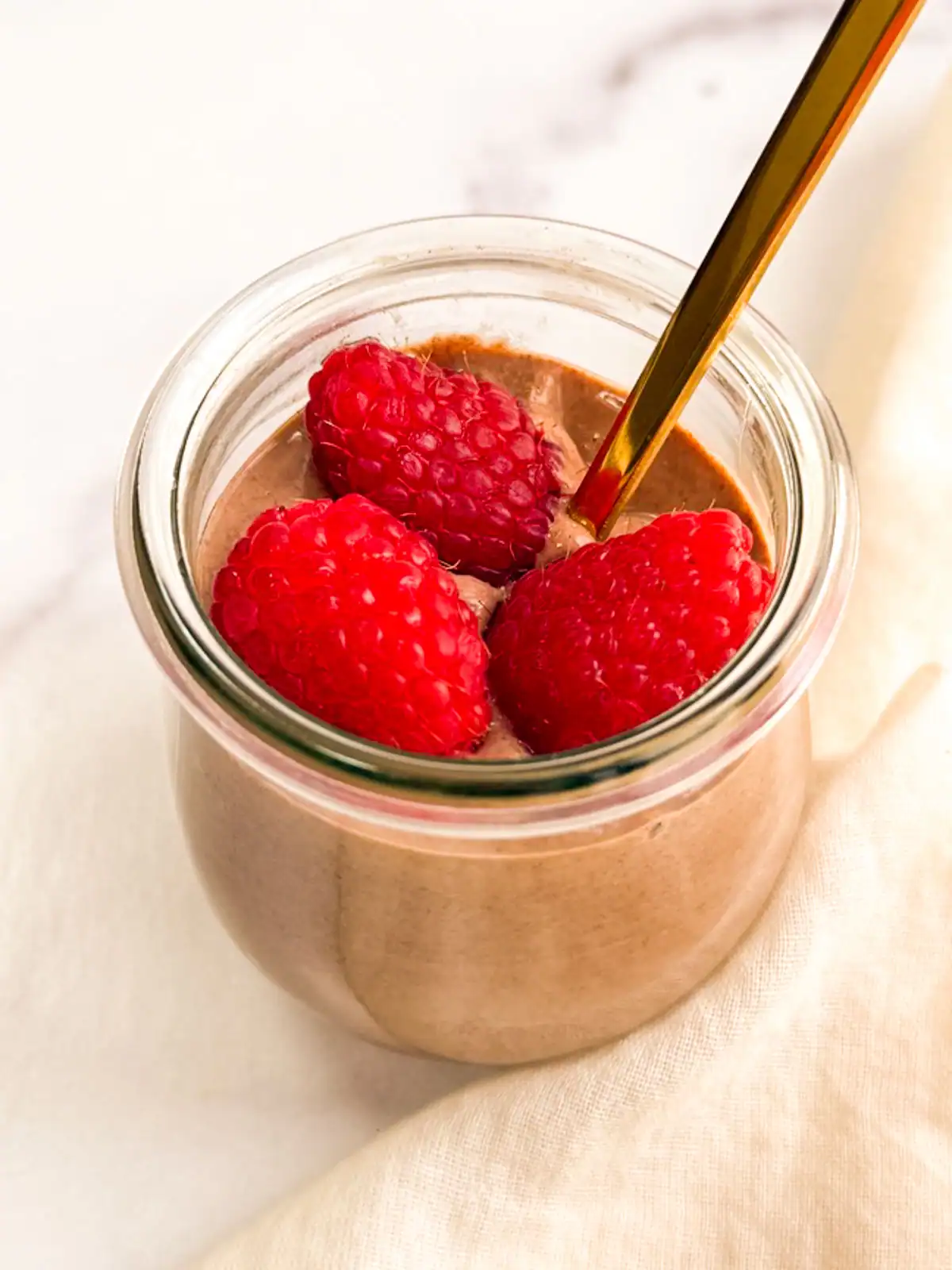 Vegan chocolate mousse topped with raspberries in a small glass jar.