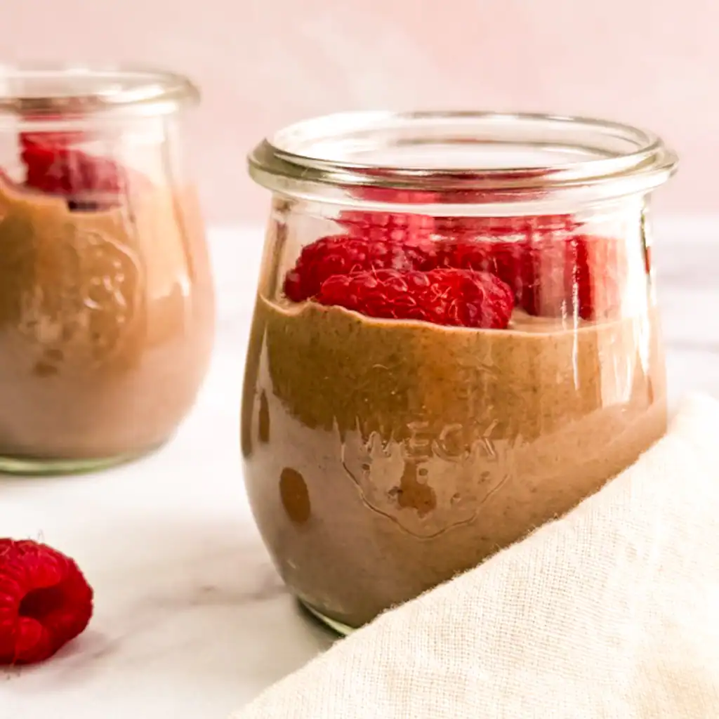 Vegan chocolate mousse topped with raspberries in small glass jars.