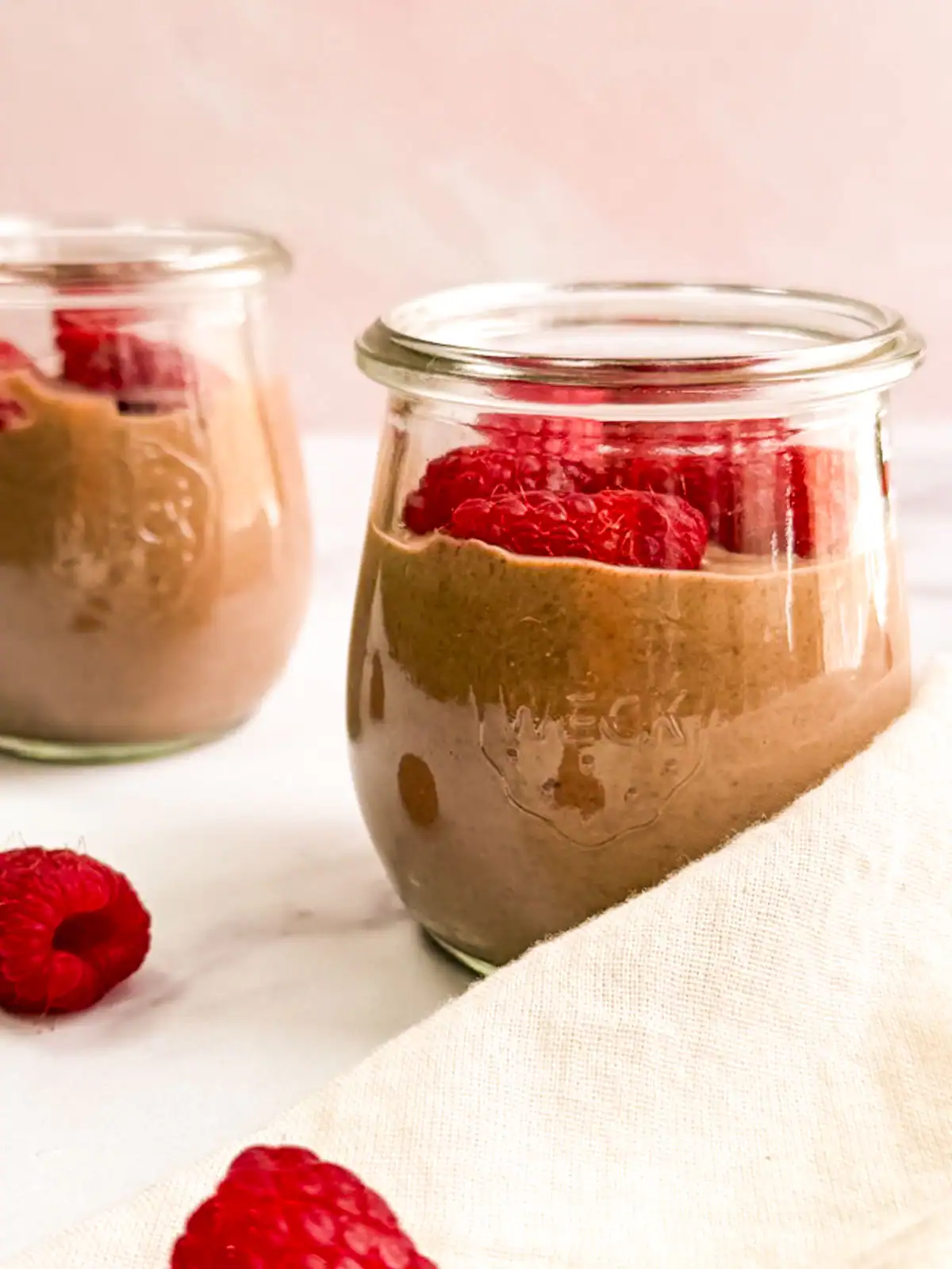 Vegan chocolate mousse topped with raspberries in small glass jars.