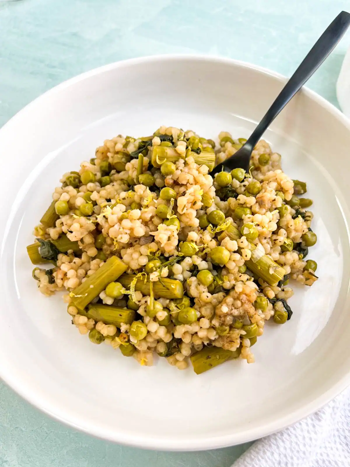 Baked pearl couscous with asparagus and peas on a white plate.