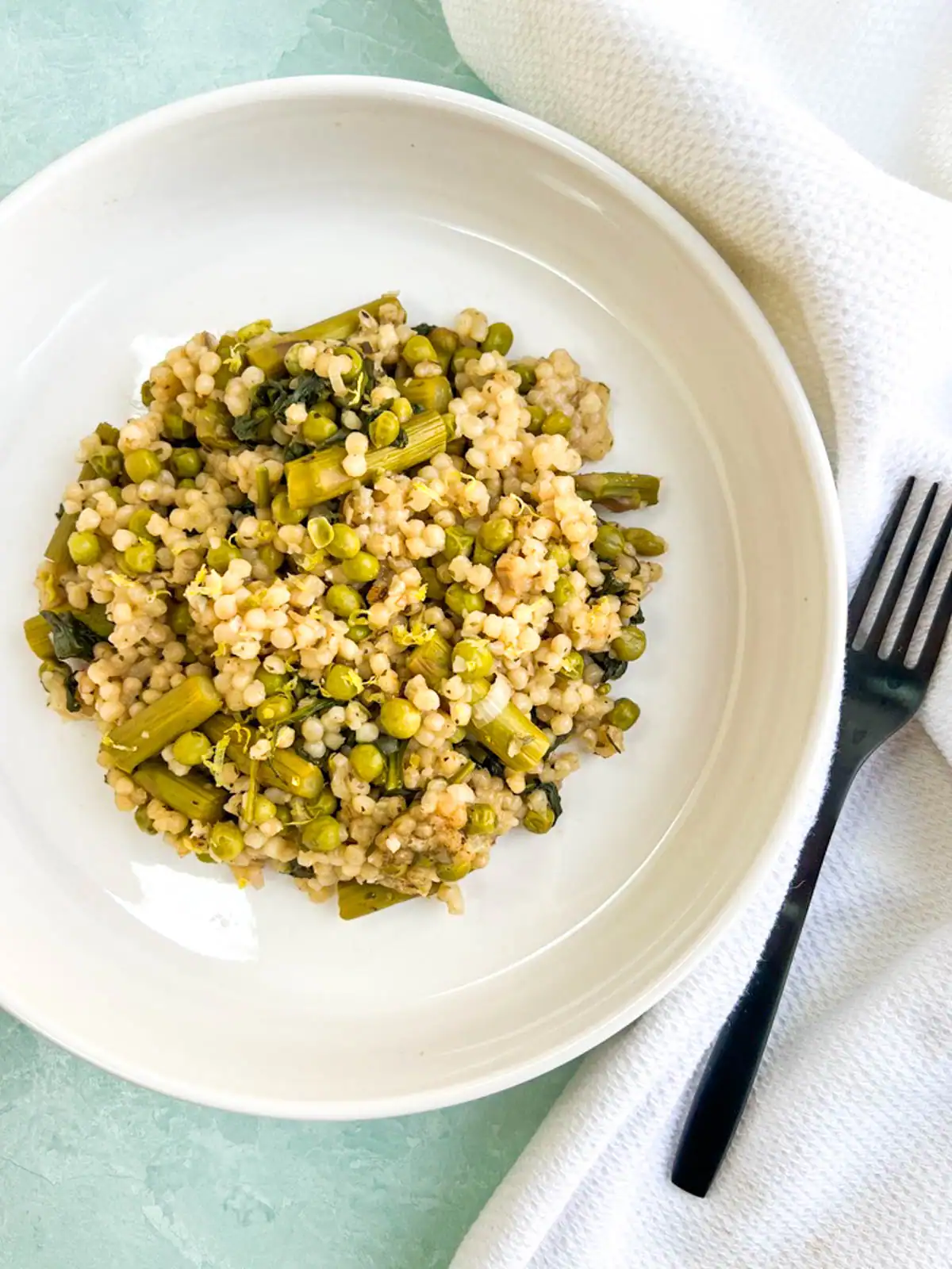 Baked pearl couscous with asparagus and peas on a white plate.