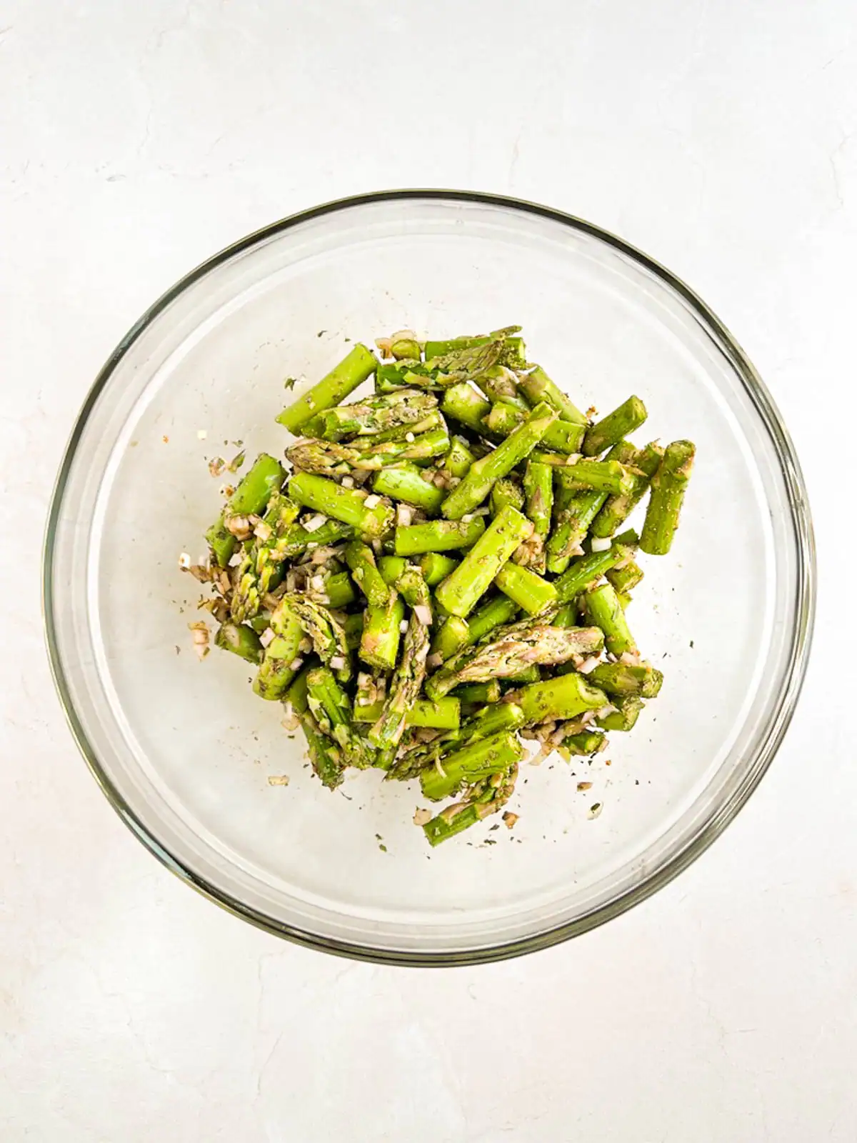 Asparagus, diced shallot, and seasoning tossed together in a glass bowl.