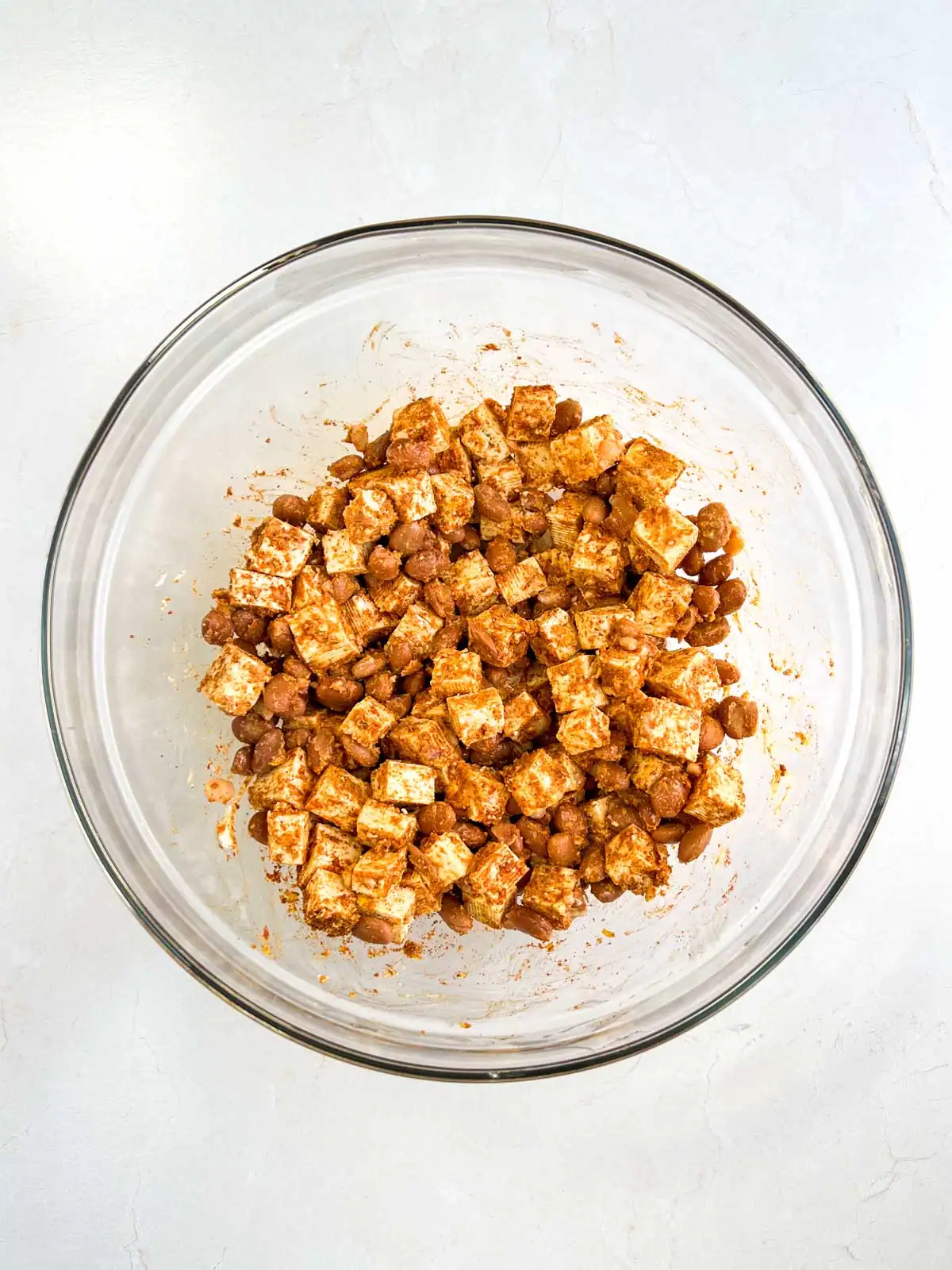 Tofu and pinto beans covered with seasoning in a glass bowl.