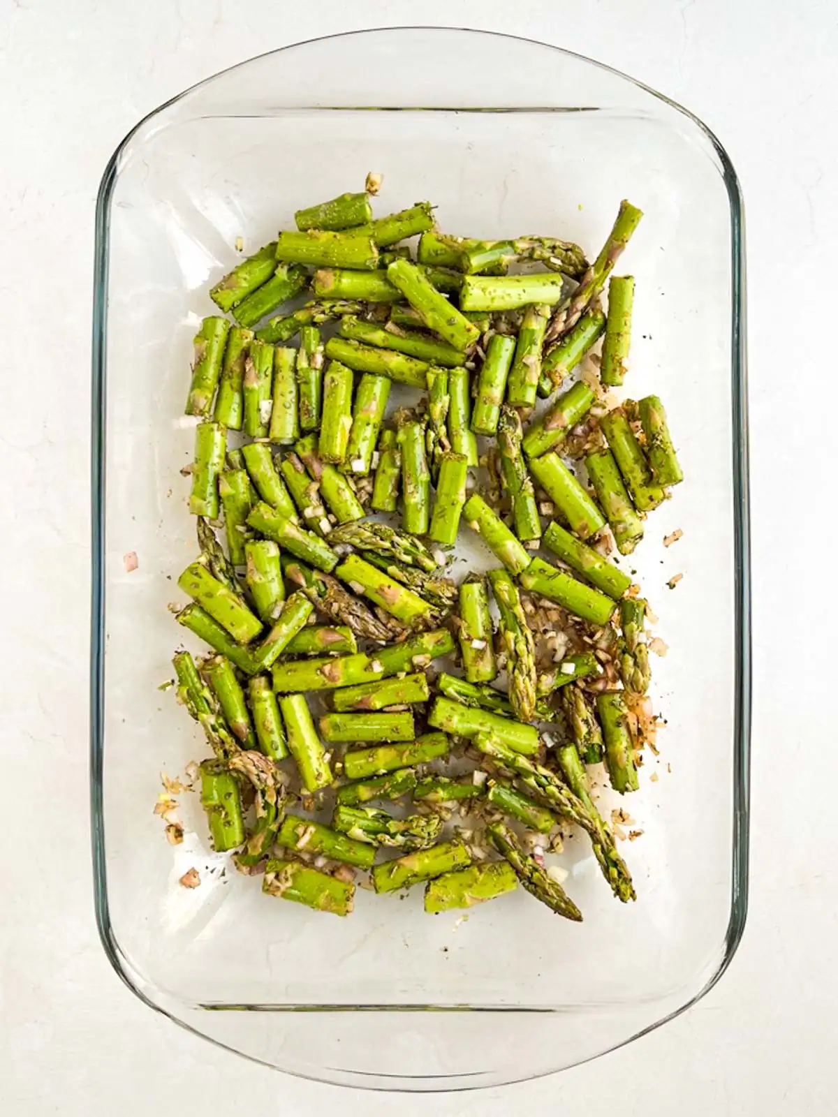 Seasoned asparagus and diced shallot in a glass casserole dish.